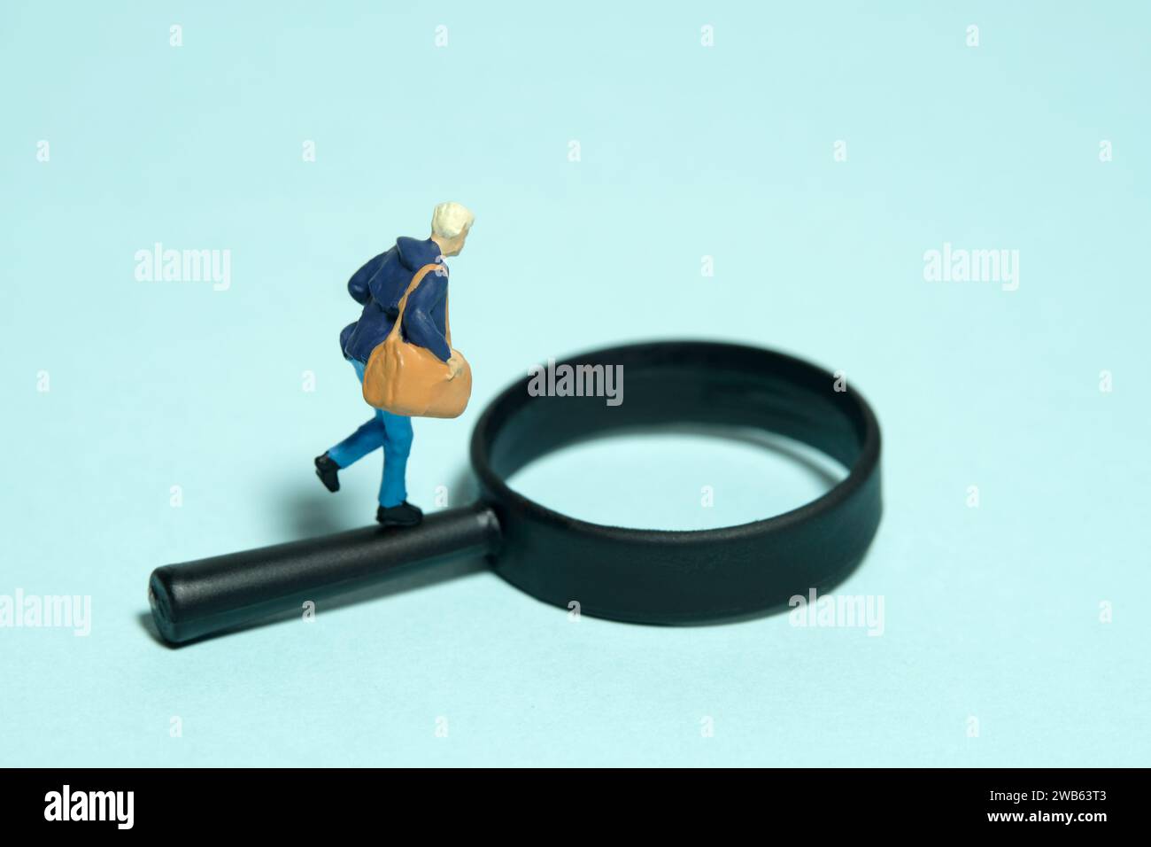 Miniatur-Kleinkinder-Spielfiguren-Fotografie. Ein Student, der über Lupe läuft. Isoliert auf blauem Hintergrund. Bild Foto Stockfoto