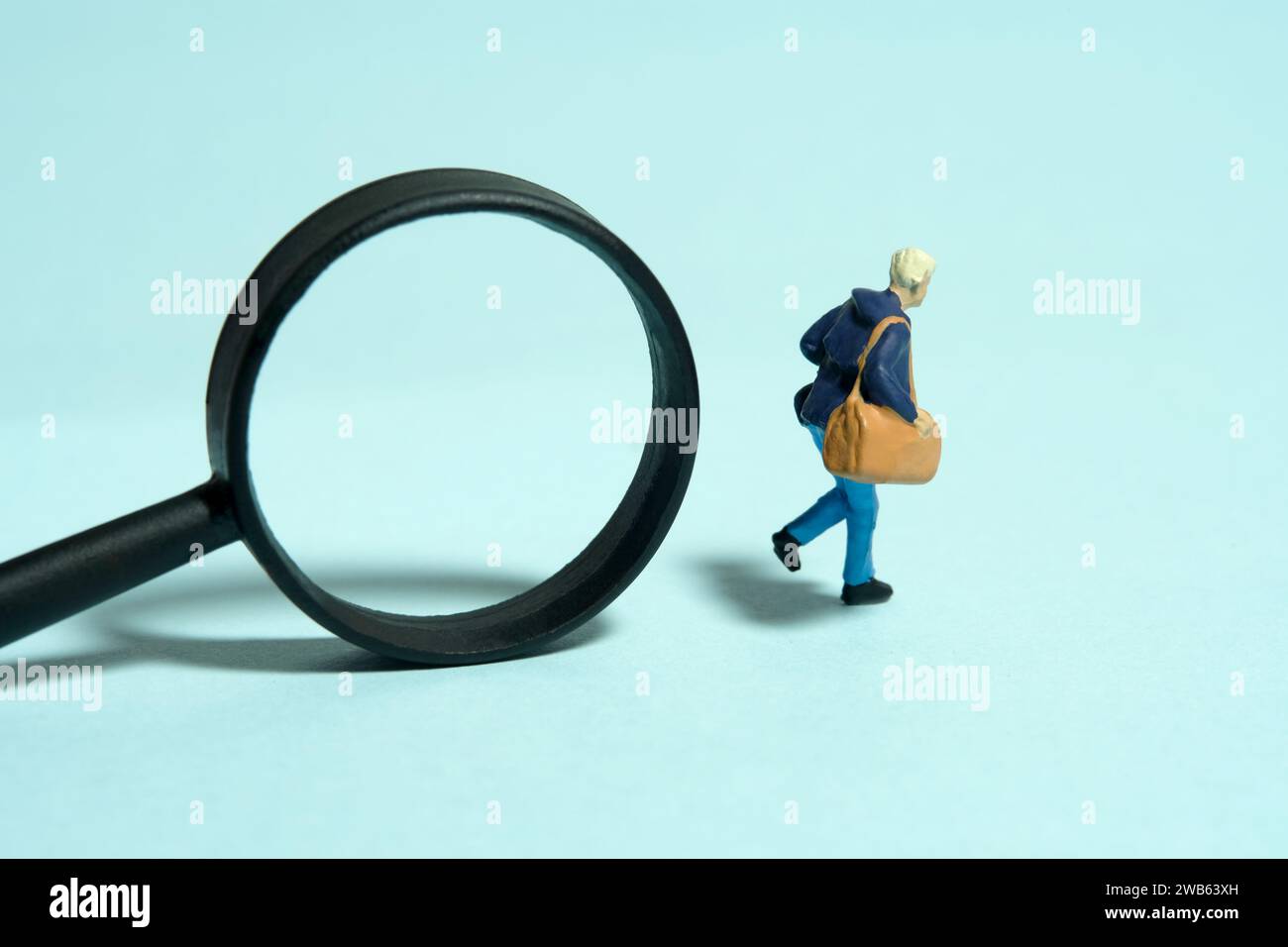 Miniatur-Kleinkinder-Spielfiguren-Fotografie. Ein Student, der vor Lupe läuft. Isoliert auf blauem Hintergrund. Bild Foto Stockfoto