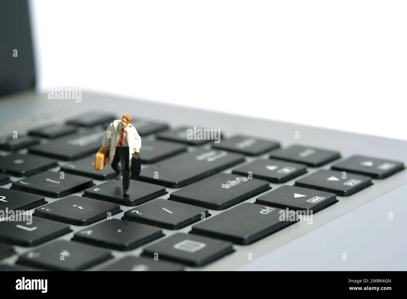 Miniatur-Kleinkinder-Spielfiguren-Fotografie. Ein Geschäftsmann, der über der Tastatur sitzt, Notebook-Laptop mit Aktentasche. Isoliert auf weißem Hintergrund. I Stockfoto
