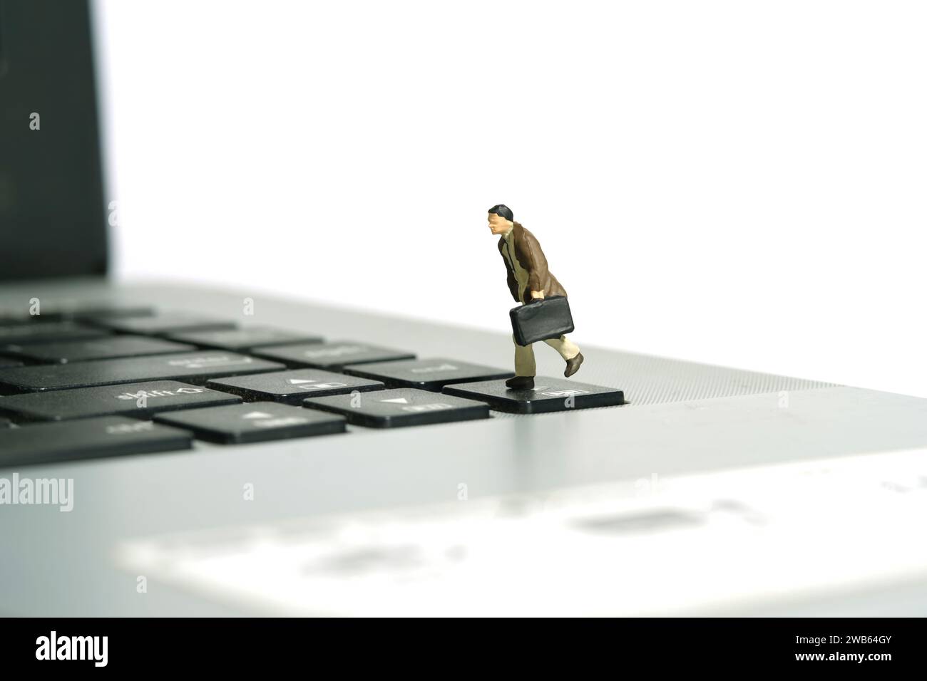 Miniatur-Kleinkinder-Spielfiguren-Fotografie. Ein Geschäftsmann, der über der Tastatur sitzt, Notebook-Laptop mit Aktentasche. Isoliert auf weißem Hintergrund. I Stockfoto