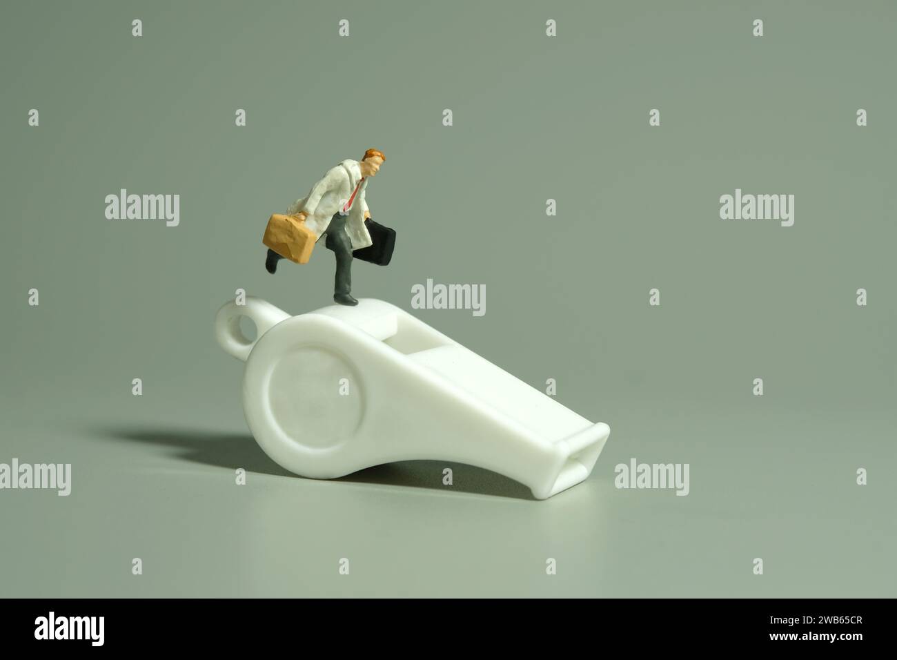 Miniaturmenschen Spielzeug-Fotografie. Illustration des Whistleblower-Konzepts. Ein Geschäftsmann, der über weißer Pfeife läuft, isoliert auf grauem Hintergrund. Stockfoto