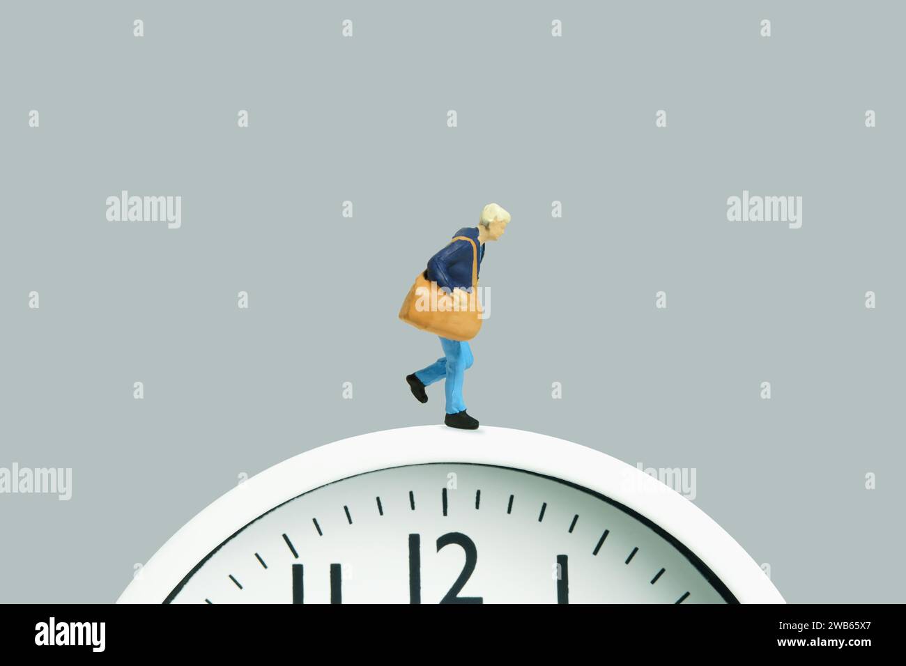 Miniatur-Kleinkinder-Spielfiguren-Fotografie. Eine Frau, die über einer schwarzen Uhr läuft und eine Reisetasche trägt. Isoliert auf grauem Hintergrund. Bild Foto Stockfoto