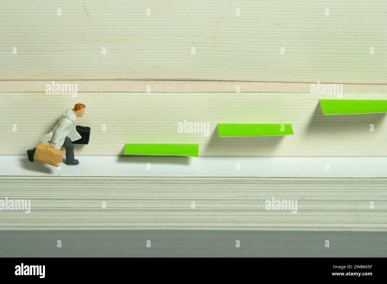 Miniatur-Kleinkinder-Spielfiguren-Fotografie. Ein Mann mit Mantel, der einen Aktenkoffer über dem Buch trägt, der auf die Treppe tritt. Bild Foto Stockfoto