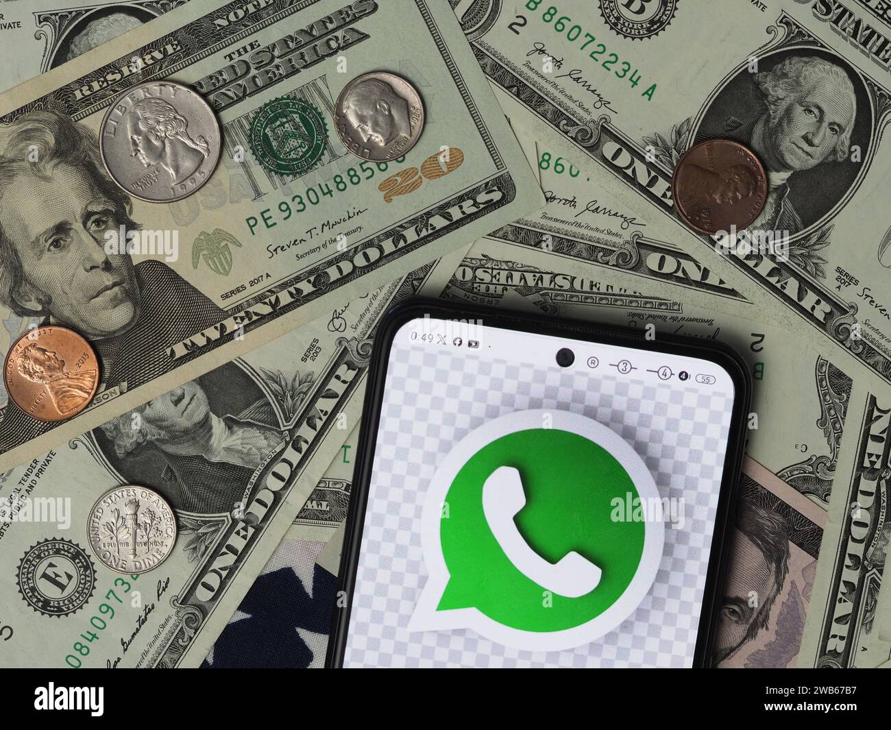 Bayern, Deutschland - 9. Januar 2024: In dieser Foto-Illustration wird ein WhatsApp-Logo auf einem Smartphone mit US-Dollar-Banknoten und Coi angezeigt Stockfoto