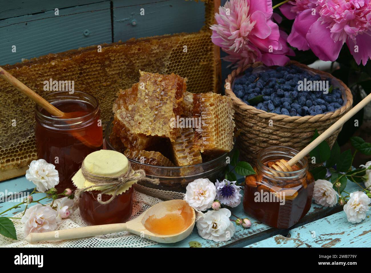 Stillleben mit natürlichem Honig, Wabenschnitt und Geißblatt-Beere mit Blumen auf hölzernem Hintergrund draußen. Ländlicher Sommer ländlicher Backg Stockfoto