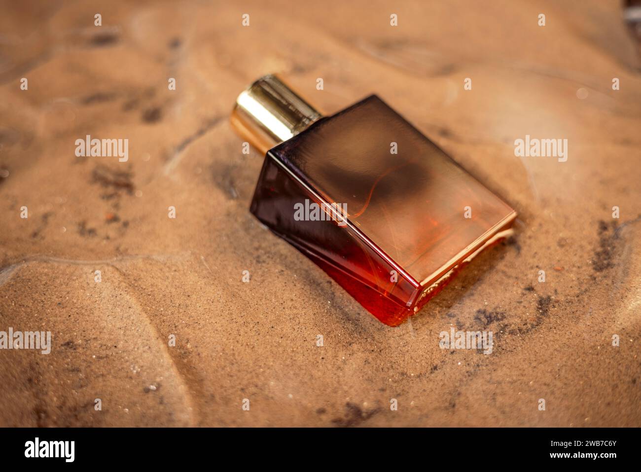 Goldene dunkelorange Flasche Luxusparfüm in nassem Sand. Stockfoto