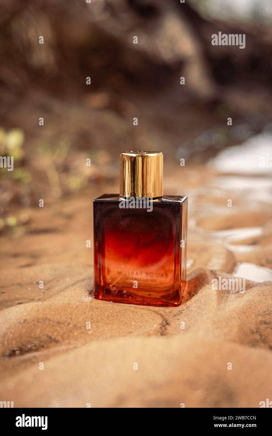 Goldene dunkelorange Flasche Luxusparfüm in nassem Sand. Stockfoto