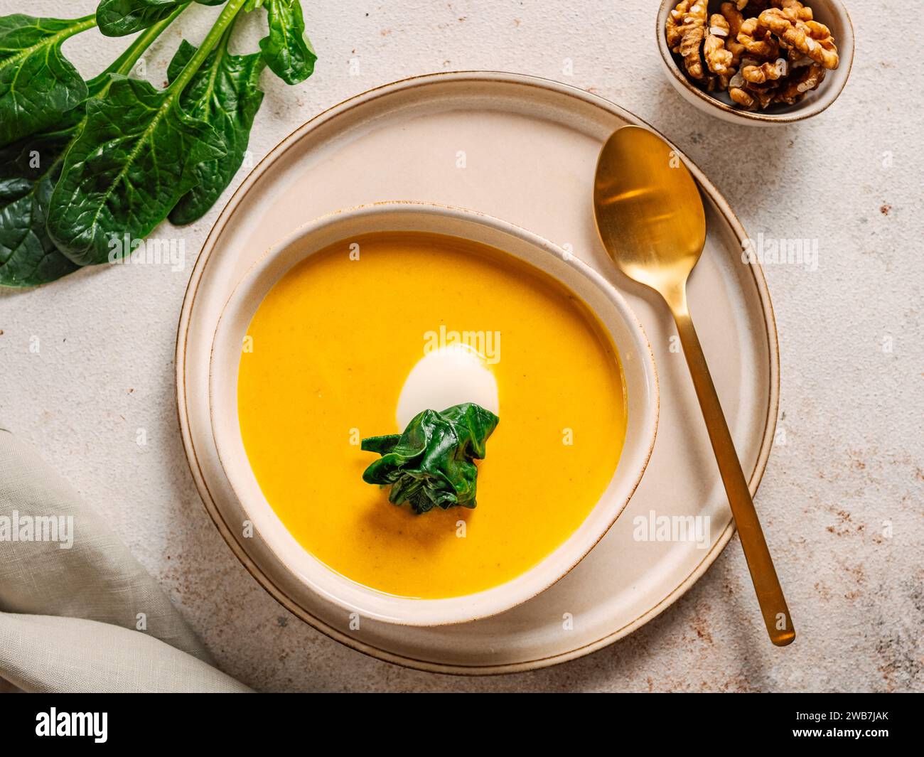 Kürbiscremesuppe serviert Spinat, Nüsse, Sauerrahm. Leckerer hausgemachter Kürbis, süße Kartoffel oder Karottensuppe in der Schüssel auf neutralem Pastelhintergrund. Gemütliche Herbstgerichte. Draufsicht Stockfoto