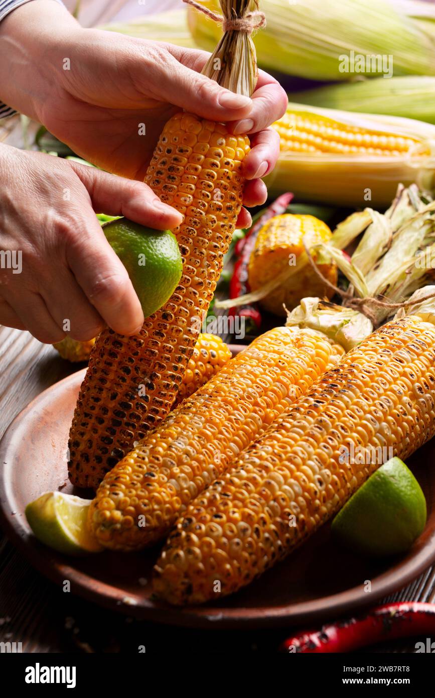 Weibliche Hände reiben einen gerösteten Maiskolben mit Limette Stockfoto