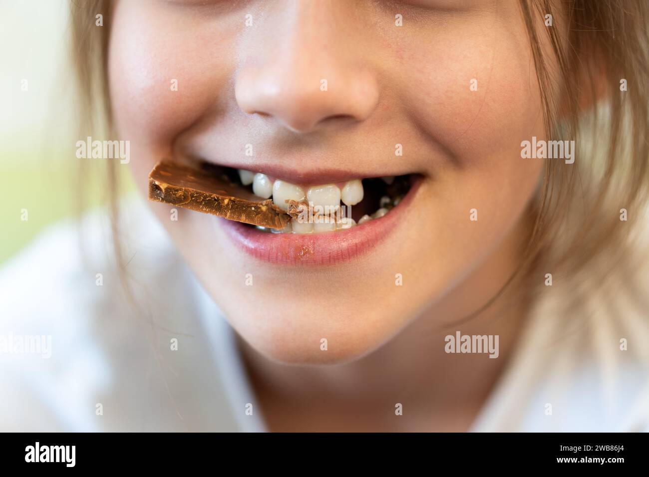 Eine detaillierte Aufnahme von einem Mädchen, das in eine Schokoladenriegel beißt. Kinderzähne beißen Schokolade Stockfoto