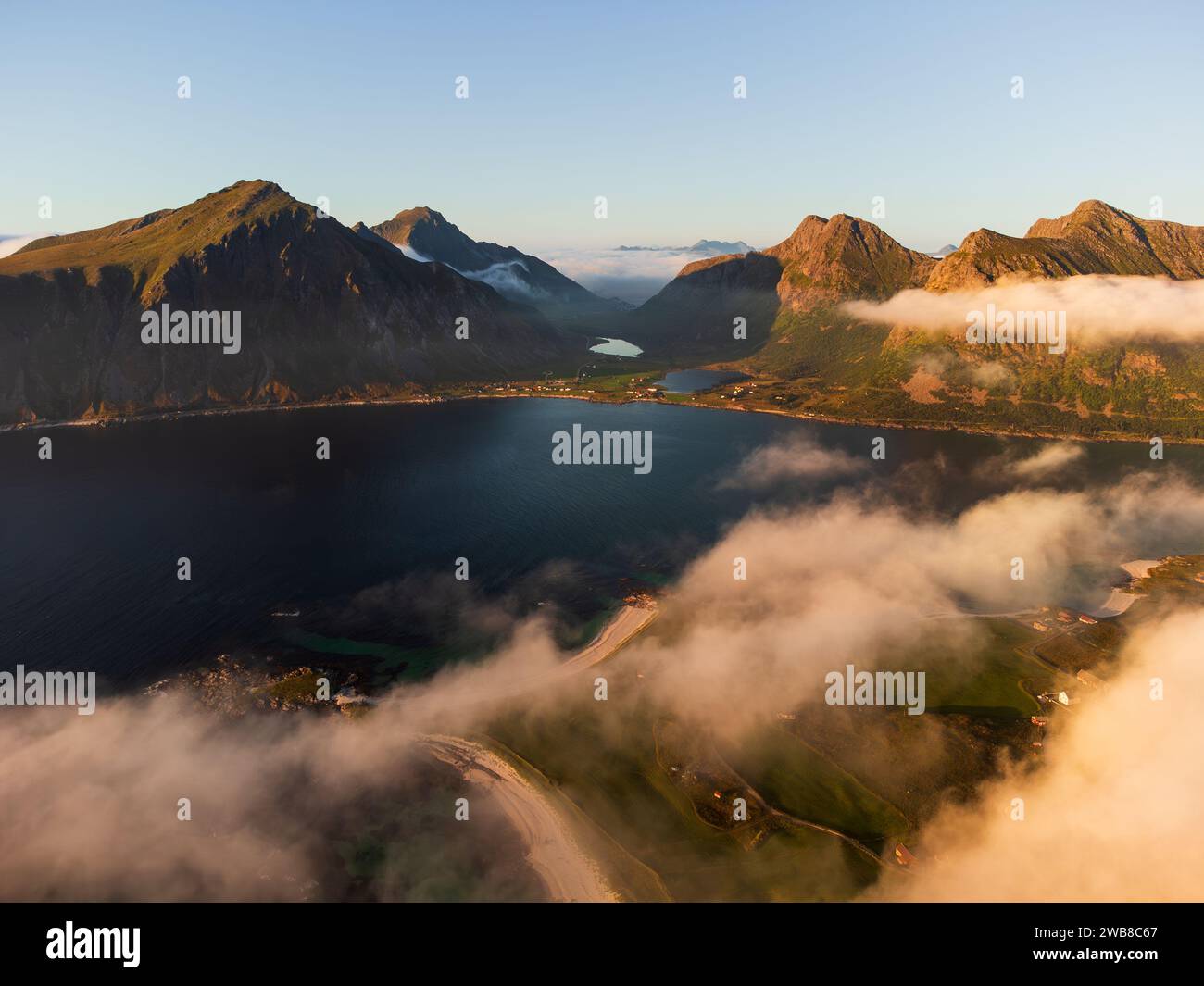Aus der Vogelperspektive der nördlichen Lofoten bei Sonnenuntergang, blauer Himmel mit flauschigem, niedrigem Nebel. Fjorde und Berge, tiefblaues Meer. Klarer Himmel oben. Stockfoto