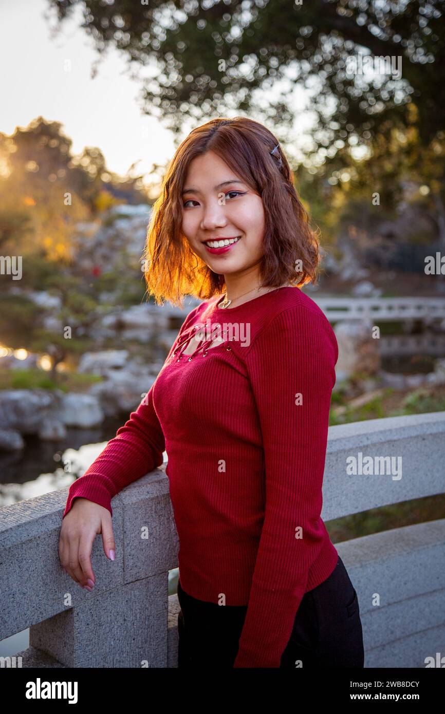 Chinese College Coed Student steht auf der Brücke bei Sonnenuntergang im Huntington's Chinese Garden Stockfoto