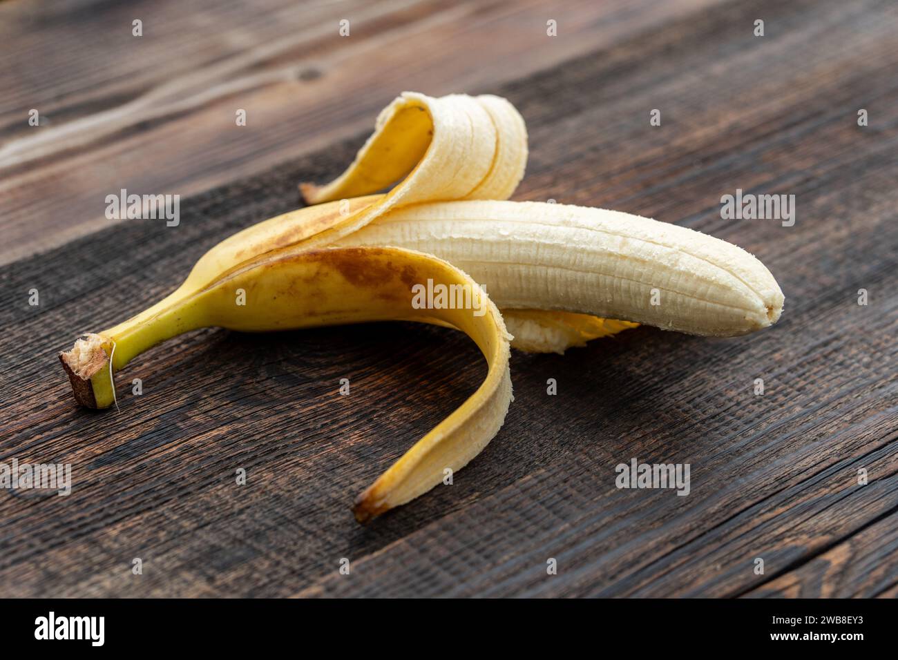 Goldene halbgeschälte Banane, die auf dem Holztisch essen kann. Eine gelbe Banane ohne Schale. Stockfoto