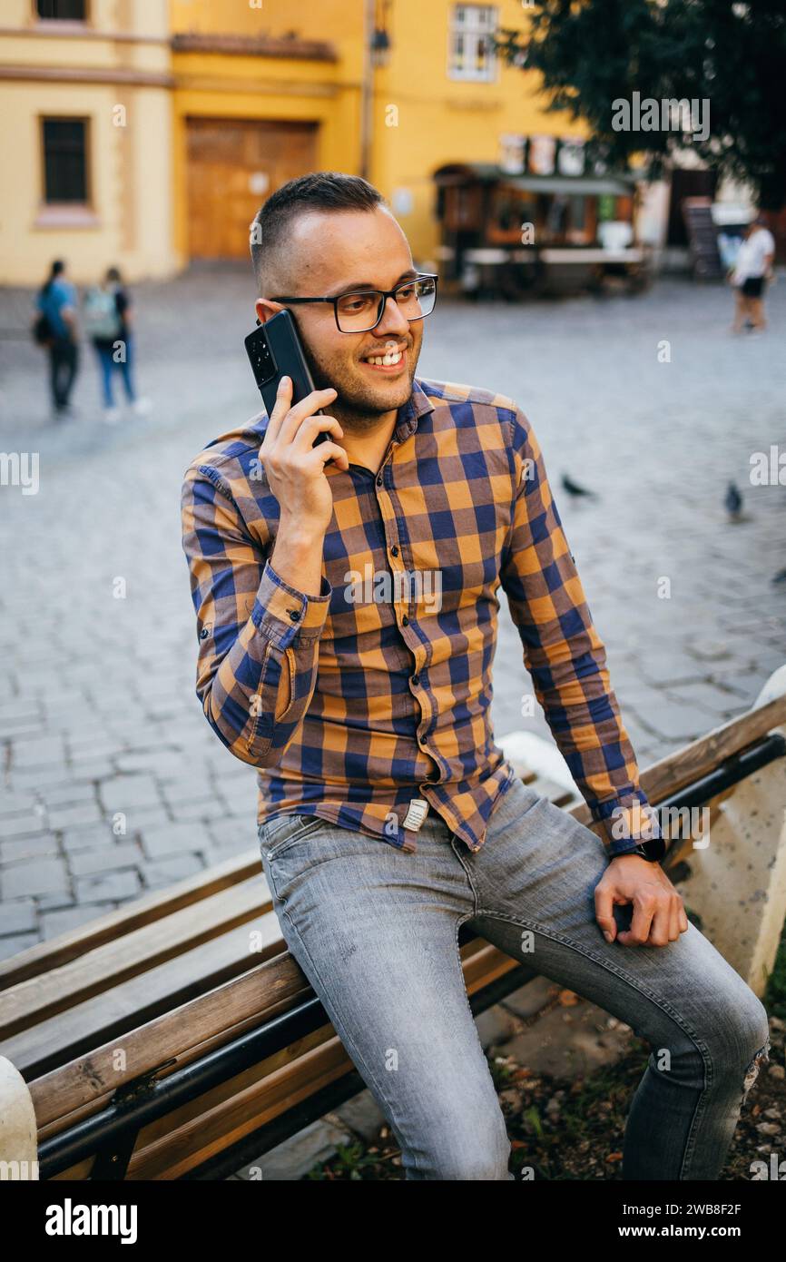 Junger Geschäftsmann im Hemd, der auf der Rückseite einer Bank sitzt und am Telefon spricht Stockfoto