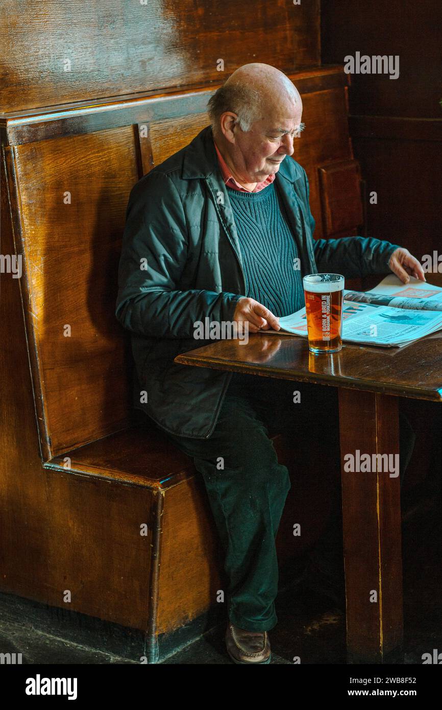 Reifer Mann trinkt Bier und liest Zeitung im Pub, Großbritannien Stockfoto