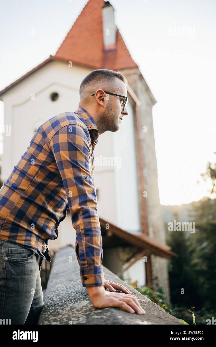 Junger Mann im Hemd und lehnt sich während einer Reise an die Burgmauer Stockfoto