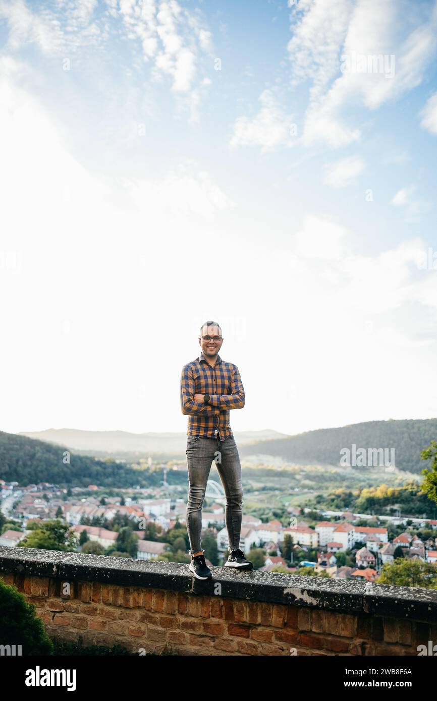 Ein junger Mann im Hemd steht lächelnd auf einer Burgmauer während einer Reise Stockfoto