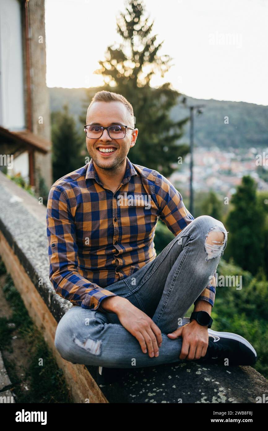 Ein junger Mann im Hemd sitzt lächelnd an einer Burgmauer Stockfoto