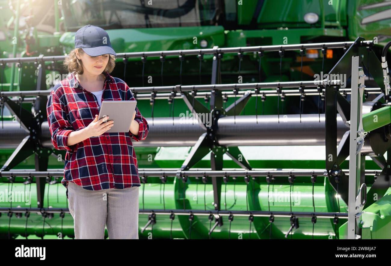 Landwirtin mit digitalem Tablet vor dem Hintergrund der Erntemaschine. Konzept der intelligenten Landwirtschaft. Stockfoto