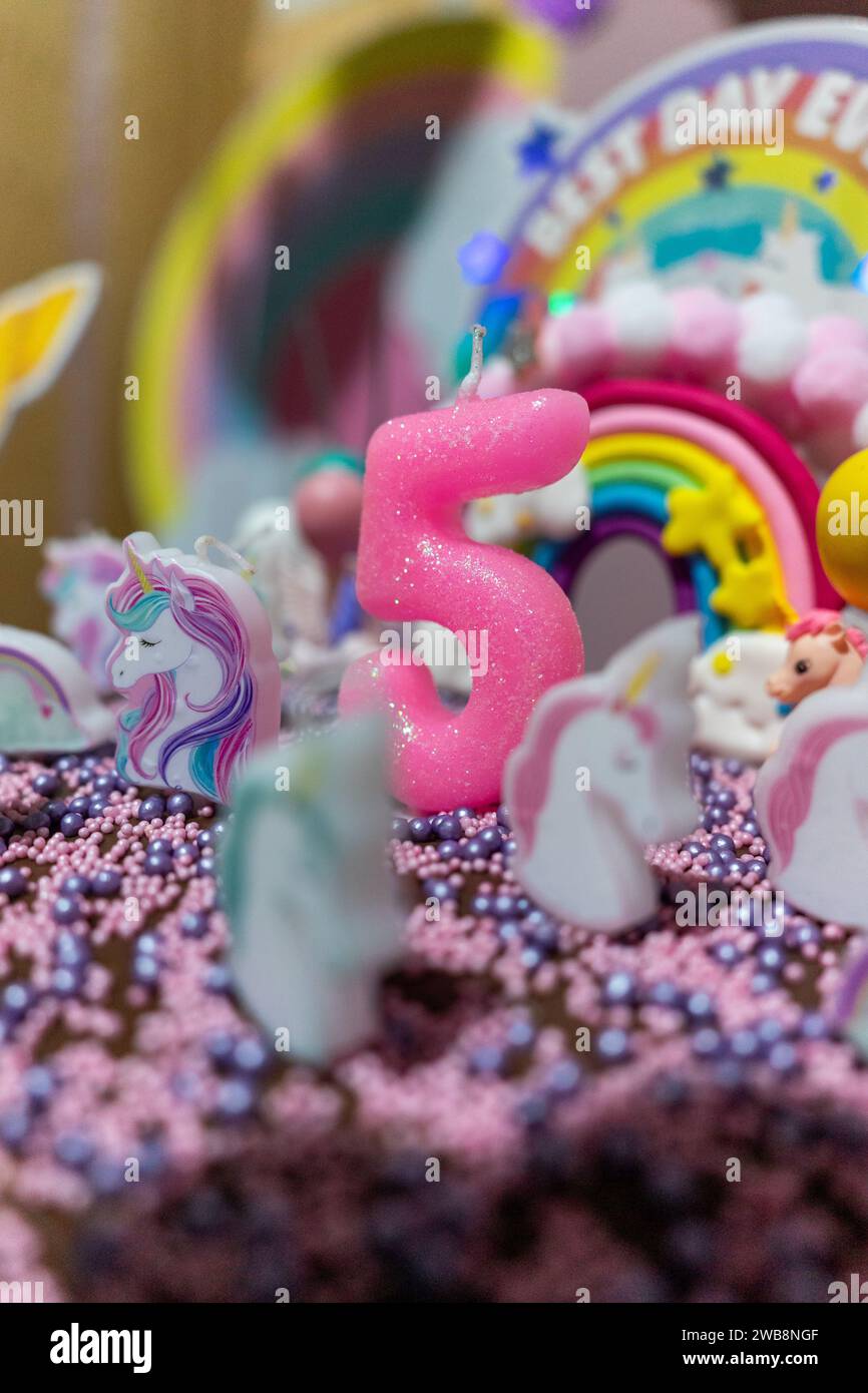 Festszene: Kerze Nummer fünf umgeben von Kerzen in Einhornform auf einer Geburtstagskuche. Stockfoto