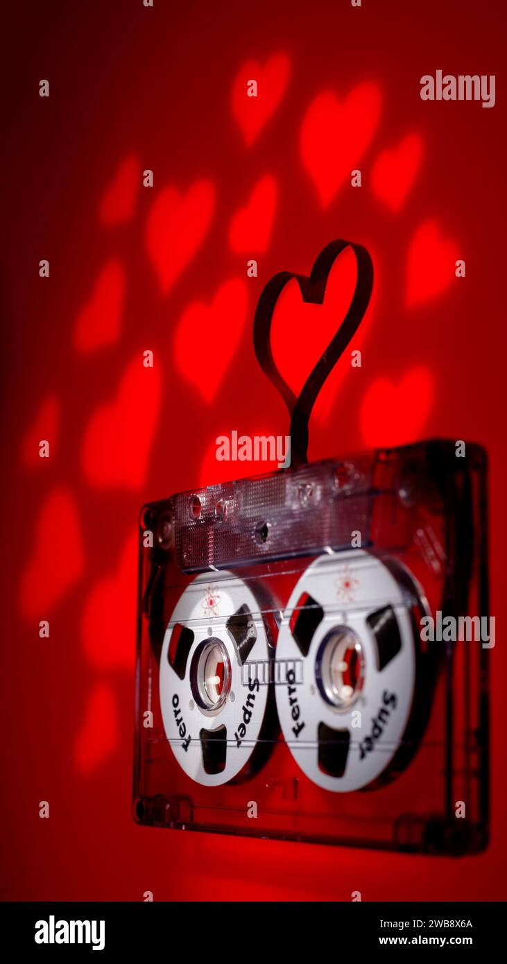 Klaipeda, Litauen - 27. Dezember 2023: Tonkassette in Nahaufnahme mit Magnetband in Herzform auf rotem Hintergrund. Vertikales Foto. Stockfoto