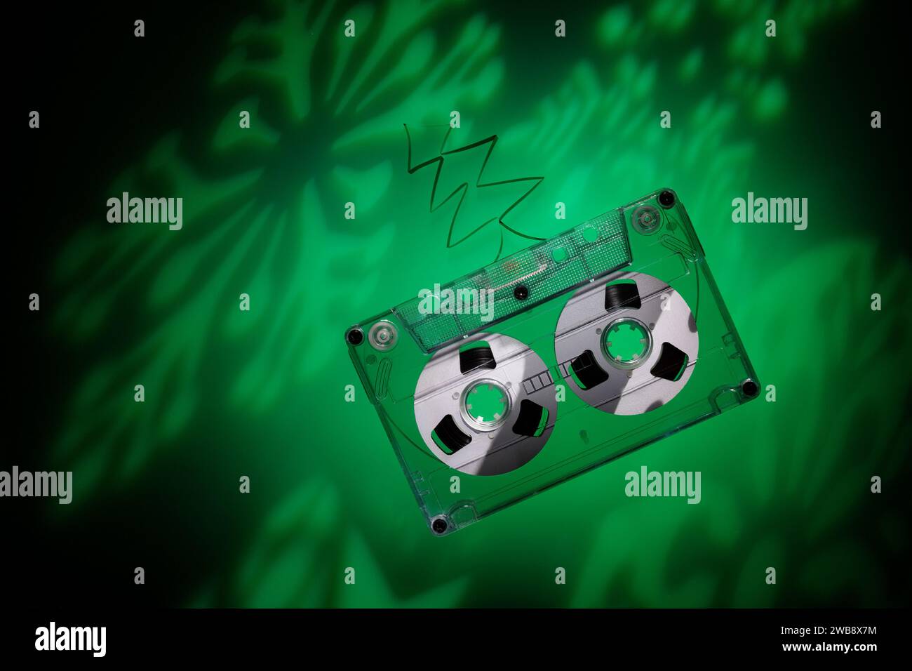 Hintergrund mit Platz für Text zum Thema Weihnachtsmusik. Grüne Schneeflockenprojektionen auf dunklem Hintergrund und eine Audiokassette. Stockfoto