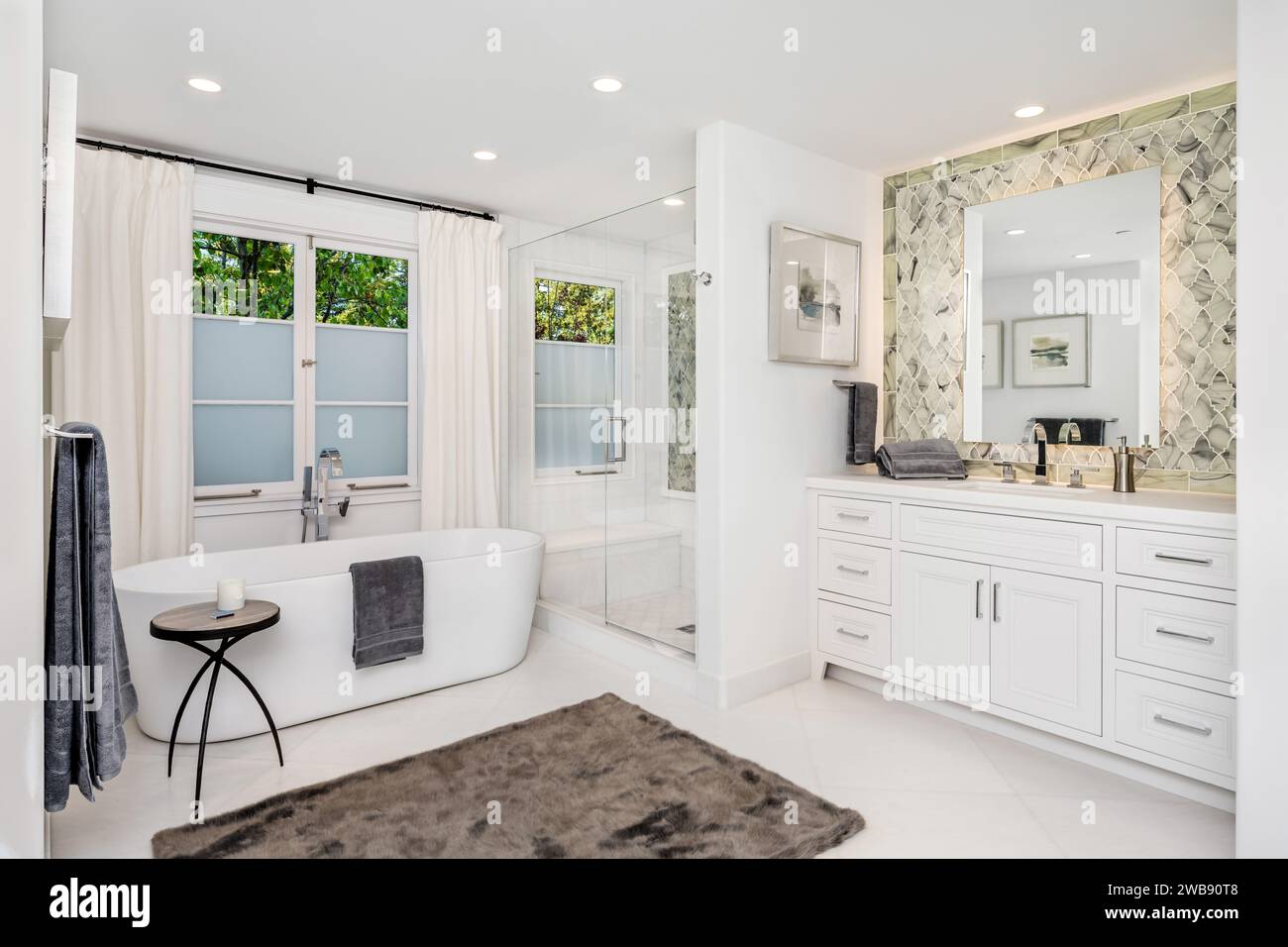 Ein makellos weißes Badezimmer mit einer großen, luxuriösen Badewanne und einem Fenster, durch das natürliches Licht in den Raum gelangt Stockfoto