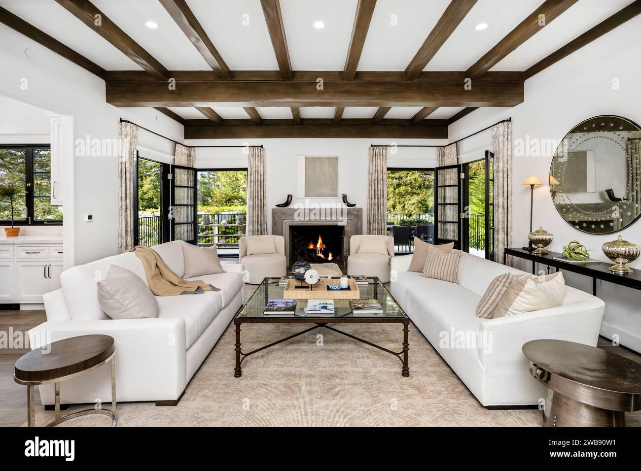 Ein modernes Wohnzimmer mit zwei weißen Sofas vor einem Kamin und großen Fenstern Stockfoto