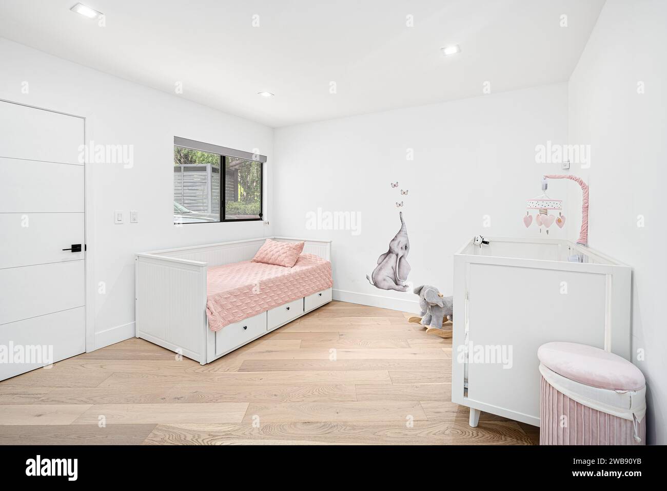 Ein gemütliches Schlafzimmer mit weiß gestrichener Wand, Twin-Size-Bett und Holzfußboden schafft eine warme und einladende Atmosphäre Stockfoto