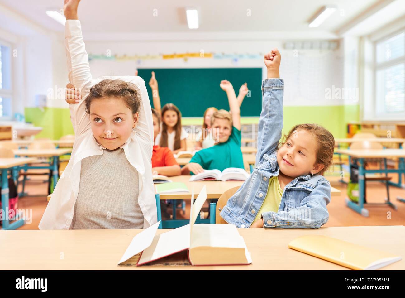 Schulmädchen heben die Hände, während sie zusammen im Klassenzimmer sitzen Stockfoto