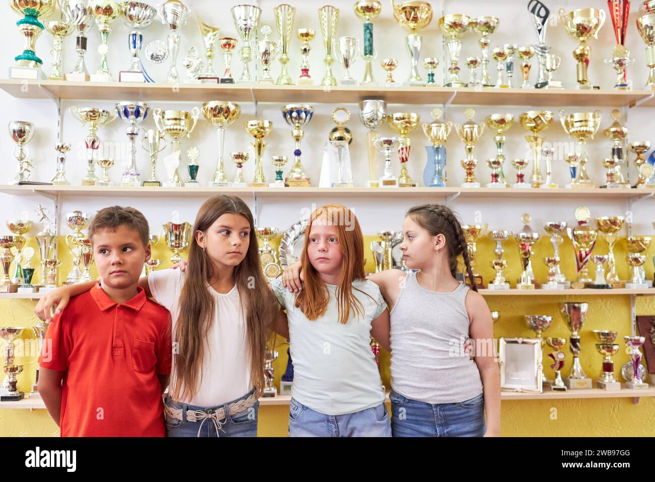 Schülerinnen und Schüler stehen mit Armen vor Trophäen im Regal der Schule Stockfoto