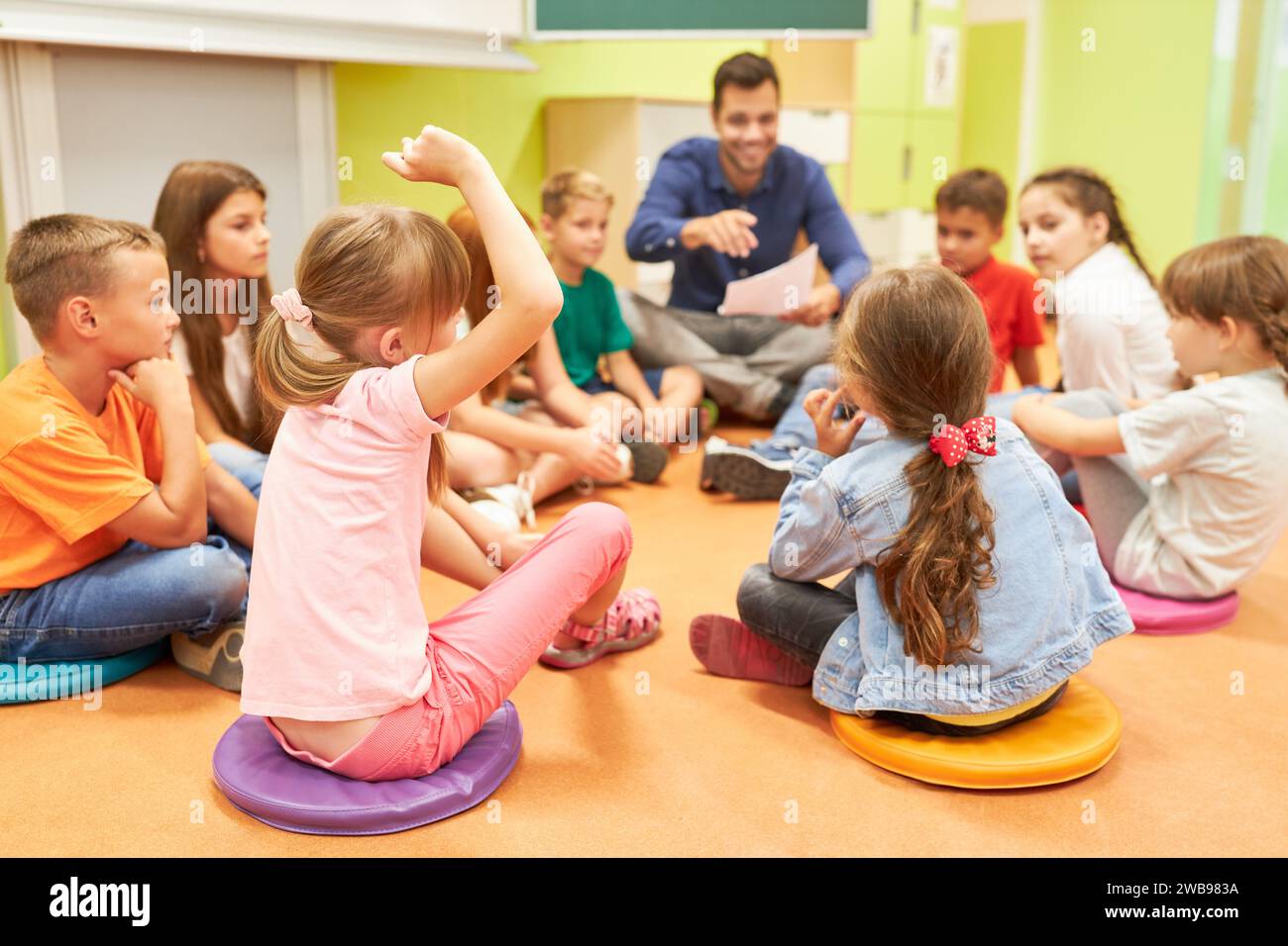 Schulkinder sitzen auf dem Boden mit männlichem Lehrer im Klassenzimmer Stockfoto