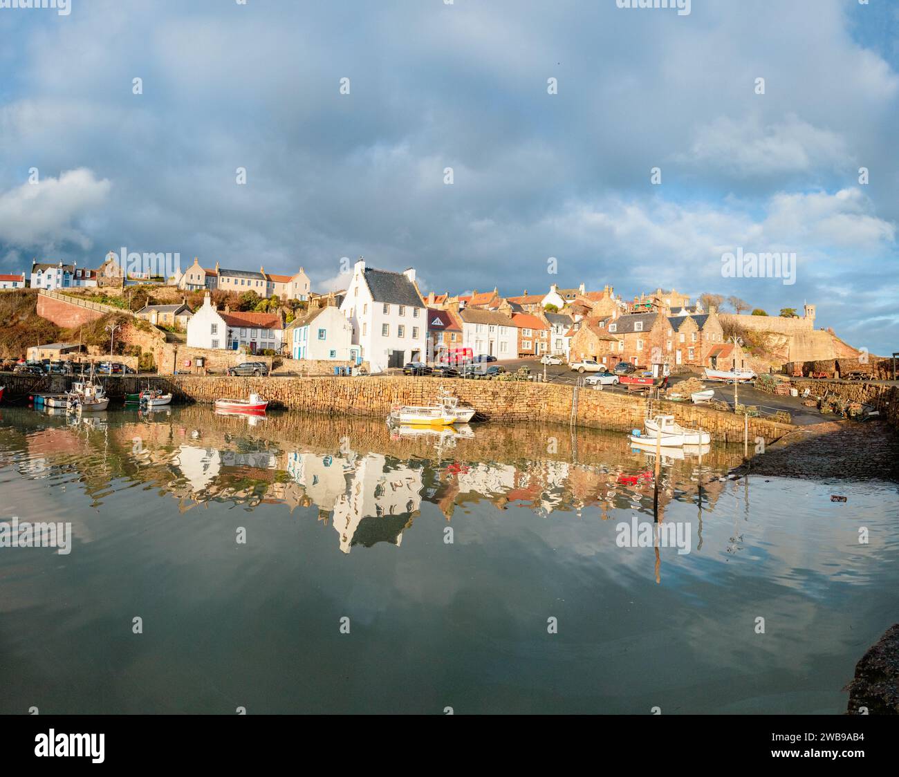 Hübscher Fischerdorfhafen und umliegende Häuser von Crail in Fife Schottland mit Booten und Reflexionen im Wasser Stockfoto