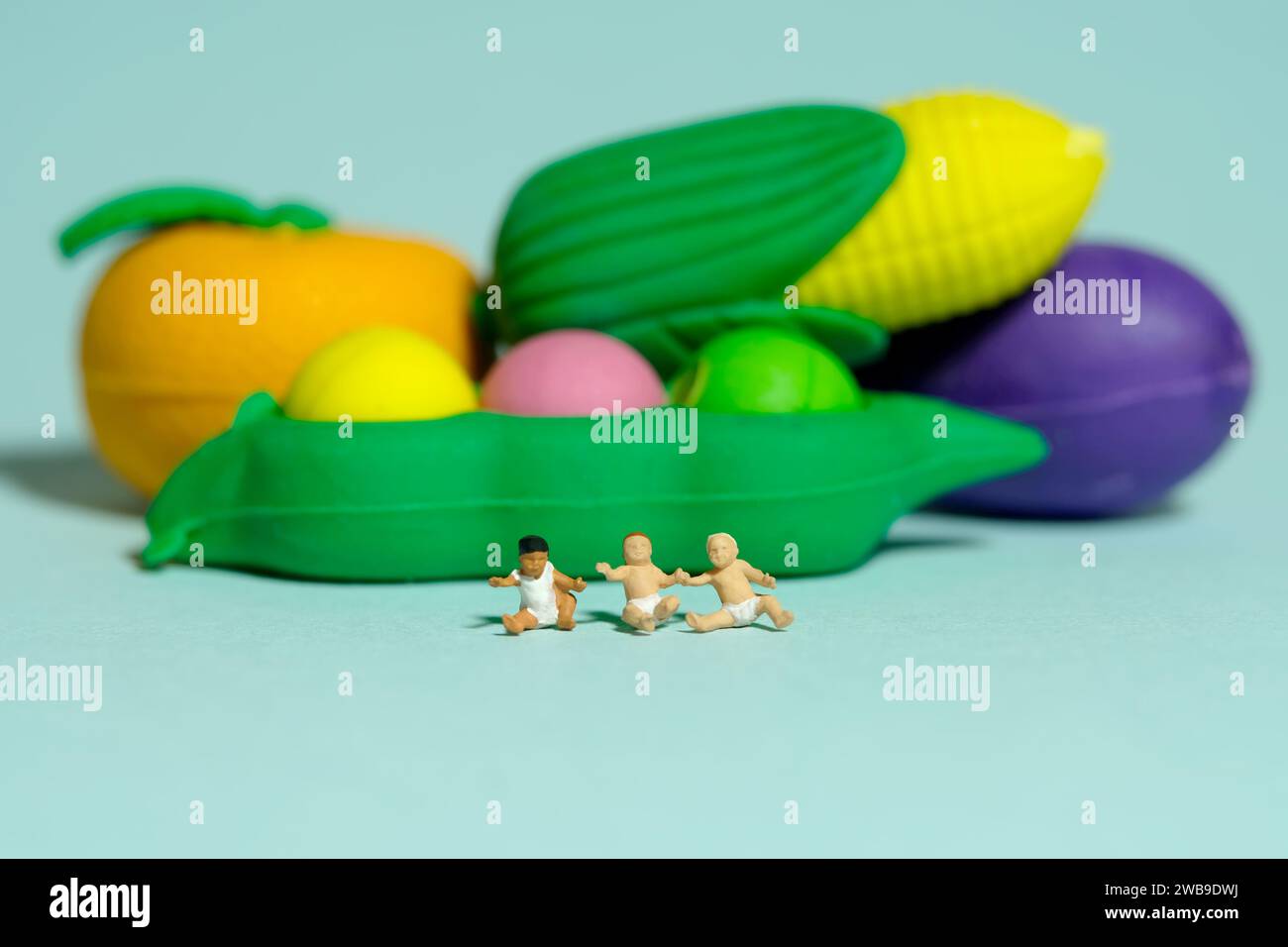 Miniatur-Kleinkinder-Spielfiguren-Fotografie. Gesunde Ernährung. Ein kleiner Junge fühlt sich glücklich, vor Gemüse zu sitzen. Isoliert auf blauem Hintergrund Stockfoto