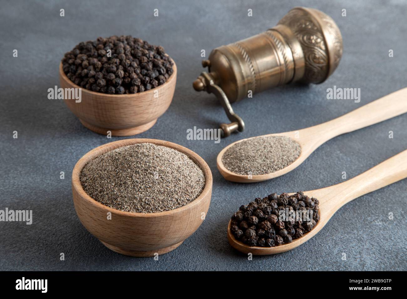 Schwarze Pfeffer, gemahlener schwarzer Pfeffer und Metallmühle auf schwarzem Hintergrund Stockfoto