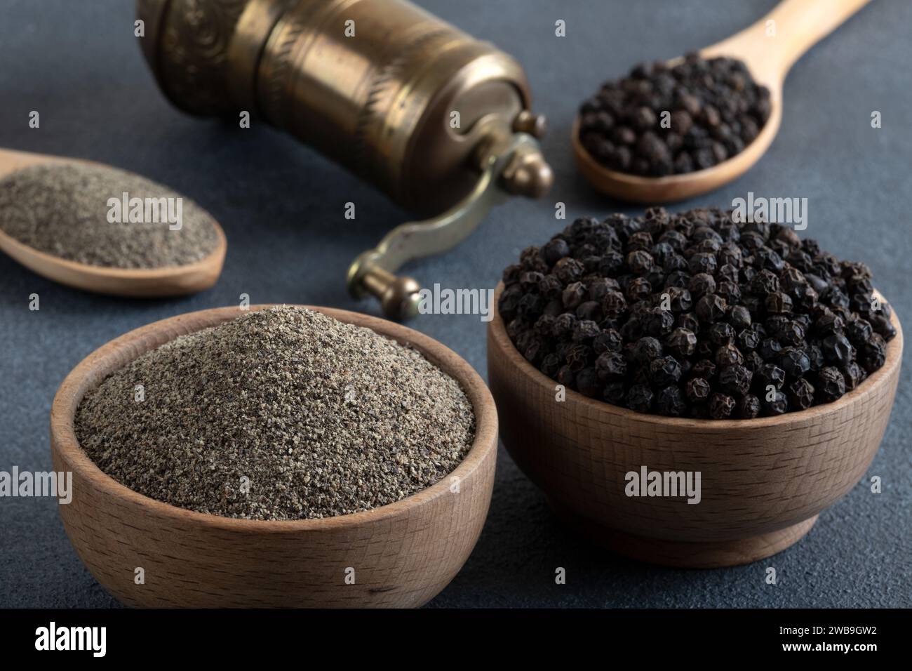 Schwarze Pfeffer, gemahlener schwarzer Pfeffer und Metallmühle auf schwarzem Hintergrund Stockfoto