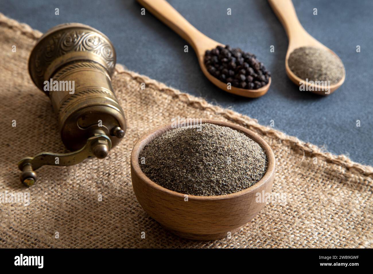 Schwarze Pfeffer, gemahlener schwarzer Pfeffer und Metallmühle auf schwarzem Hintergrund Stockfoto