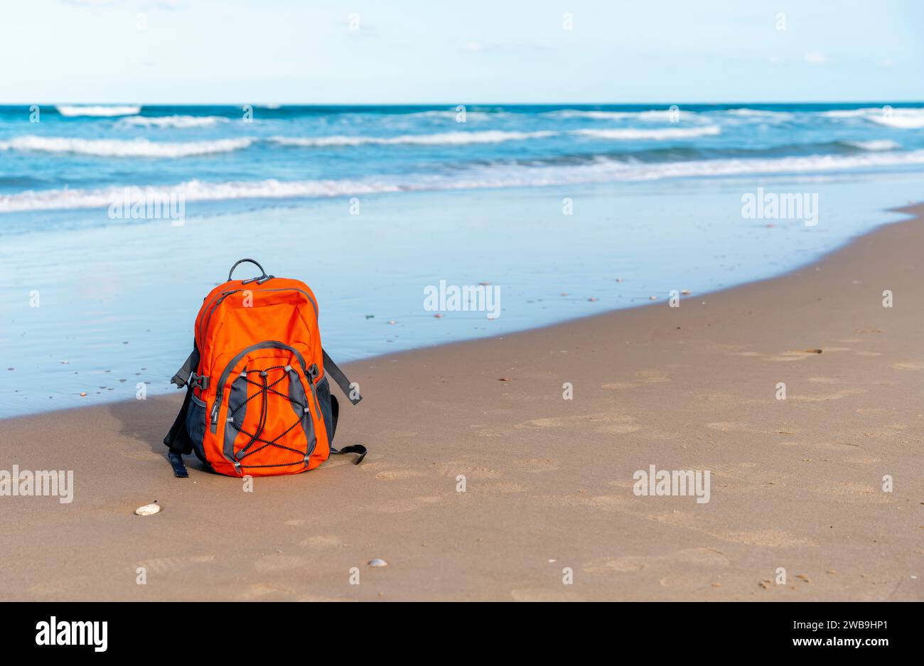 Oranger Rucksack am Meer gegen Meer bei traumhaftem Wetter. Reiseversicherungskonzept. Leichte Fahrt Stockfoto