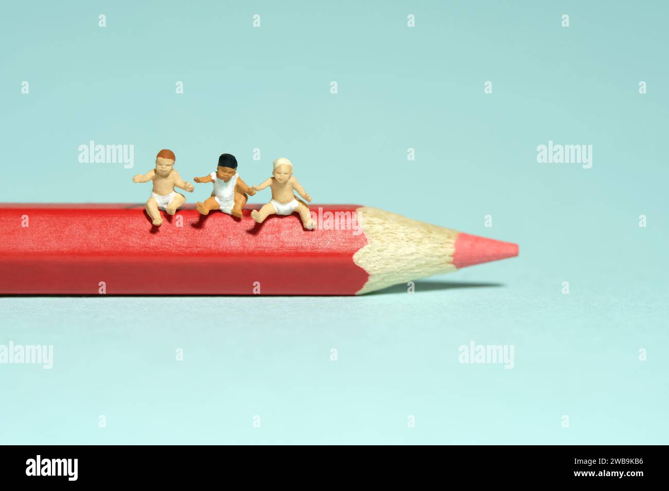 Miniatur-Kleinkinder-Spielfiguren-Fotografie. Kunststudium und Lernkonzept. Eine Gruppe von Kleinkindern, die über der Farbe des roten Bleistifts sitzen. Isoliert auf blauem B Stockfoto
