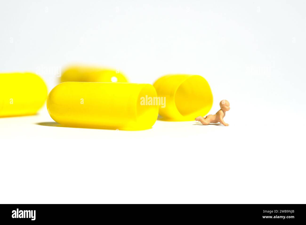 Miniatur-Kleinkinder-Spielfiguren-Fotografie. Ein neugeborenes Baby, das aus dem Inneren der gelben Arzneimittelpille herauskriecht. Isoliert auf weißem Hintergrund. Im Stockfoto