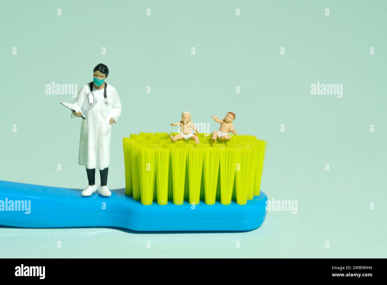 Miniatur-Kleinkinder-Spielfiguren-Fotografie. Zwei kleine Jungen, jammernd, sitzen über der Zahnbürste neben der Ärztin. Isoliert auf grünem Hintergrund Stockfoto