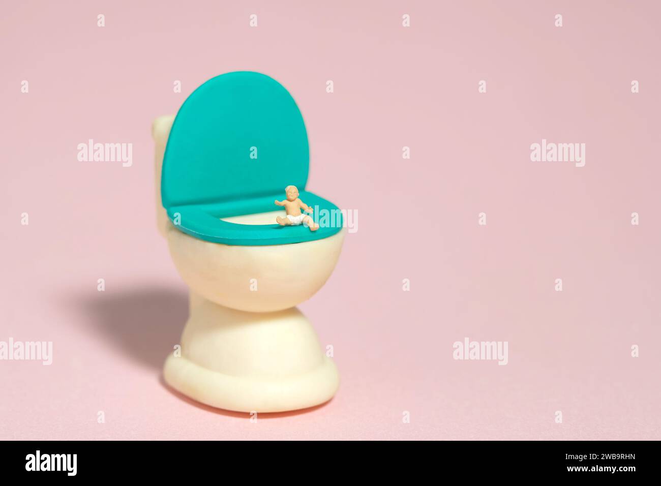 Miniatur-Kleinkinder-Spielfiguren-Fotografie. Ein Junge, Kleinkind, das wimmt, Sitz über dem Töpfchen-WC-Schrank. Isoliert auf rosafarbenem Hintergrund. Bildfoto Stockfoto