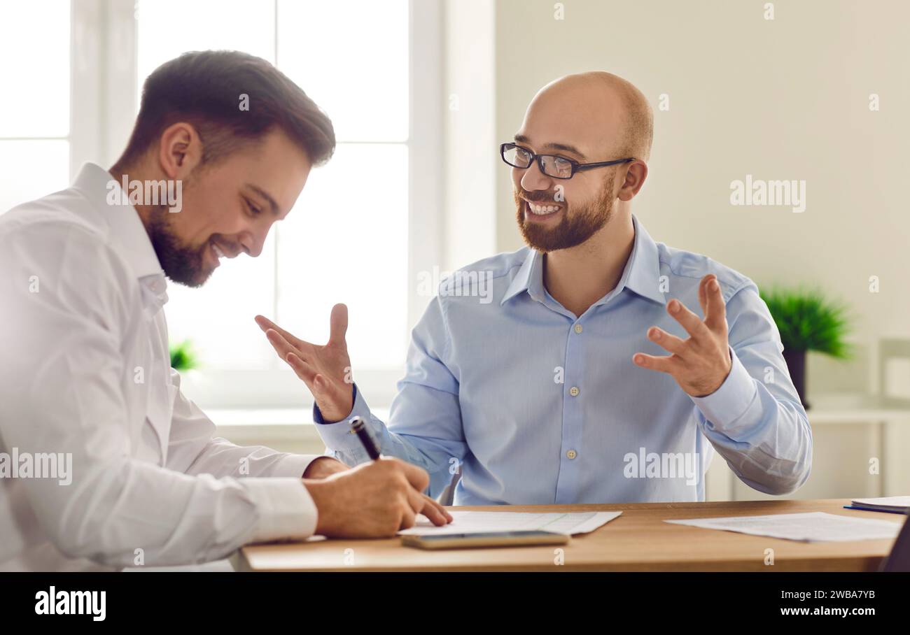 Zwei lächelnde Geschäftsleute sitzen zusammen am Schreibtisch im Büro und arbeiten an Dokumenten Stockfoto