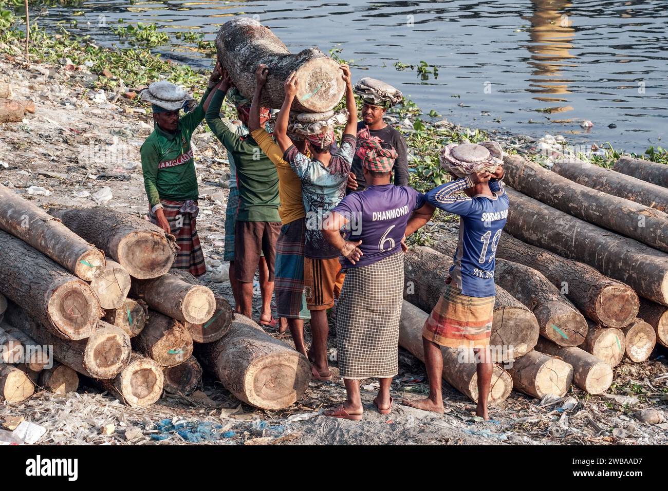 Träger transportieren schwere Baumstämme am Ufer des Buriganga River in Dhaka Bangladesch Stockfoto