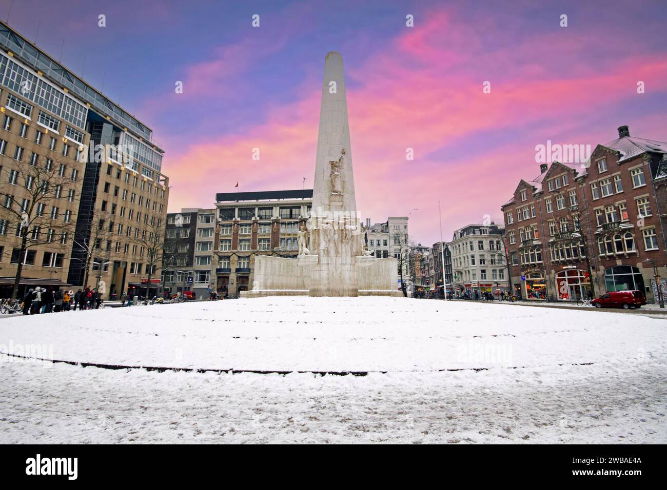 Verschneite Damplatz in Amsterdam Niederlande mit dem Nationaldenkmal im Winter bei Sonnenuntergang Stockfoto