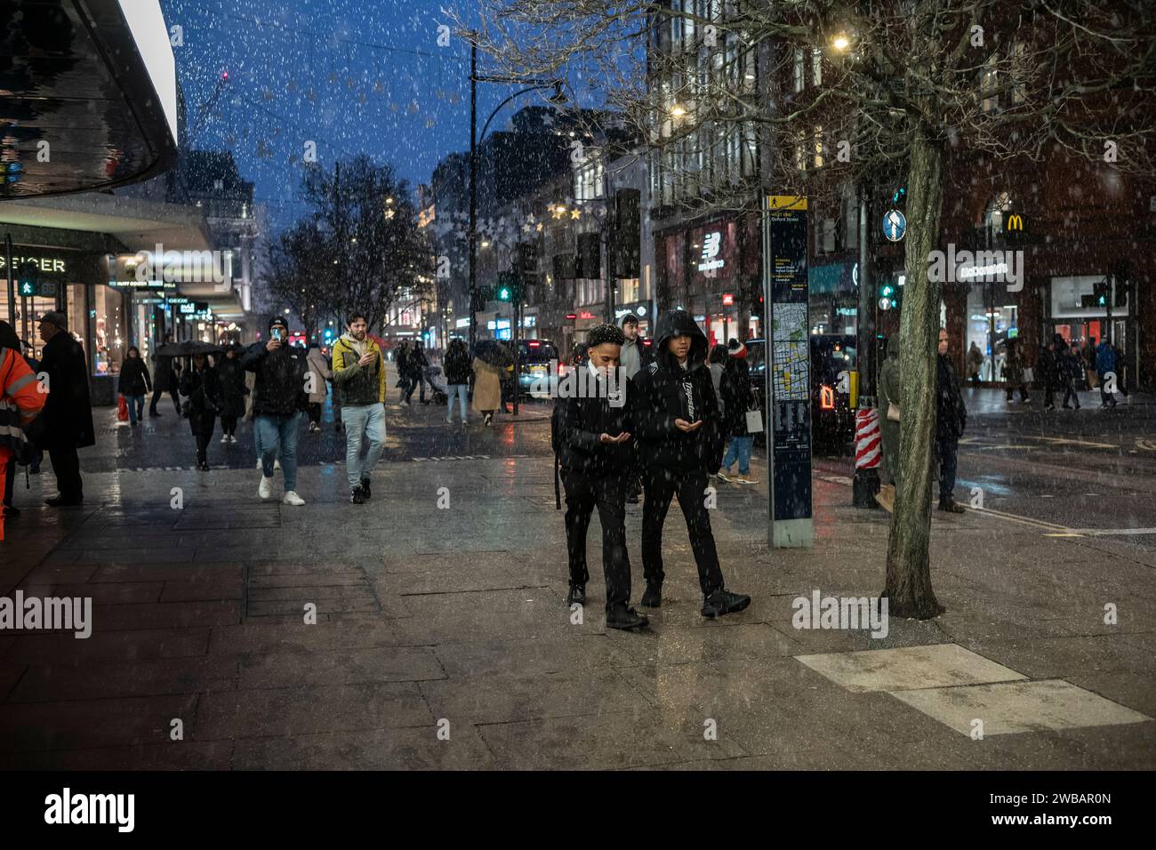 Käufer trotzen dem kalten Winter bei eisigen Schneeregen und Regenschauern auf der Oxford Street, Londons geschäftigster High Street, England, Großbritannien Stockfoto