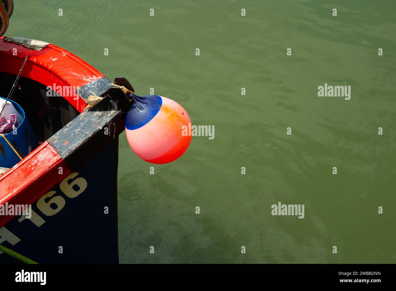 Nahaufnahme eines orangefarbenen Kotflügels am Bug eines Bootes mit grünem Wasser Stockfoto