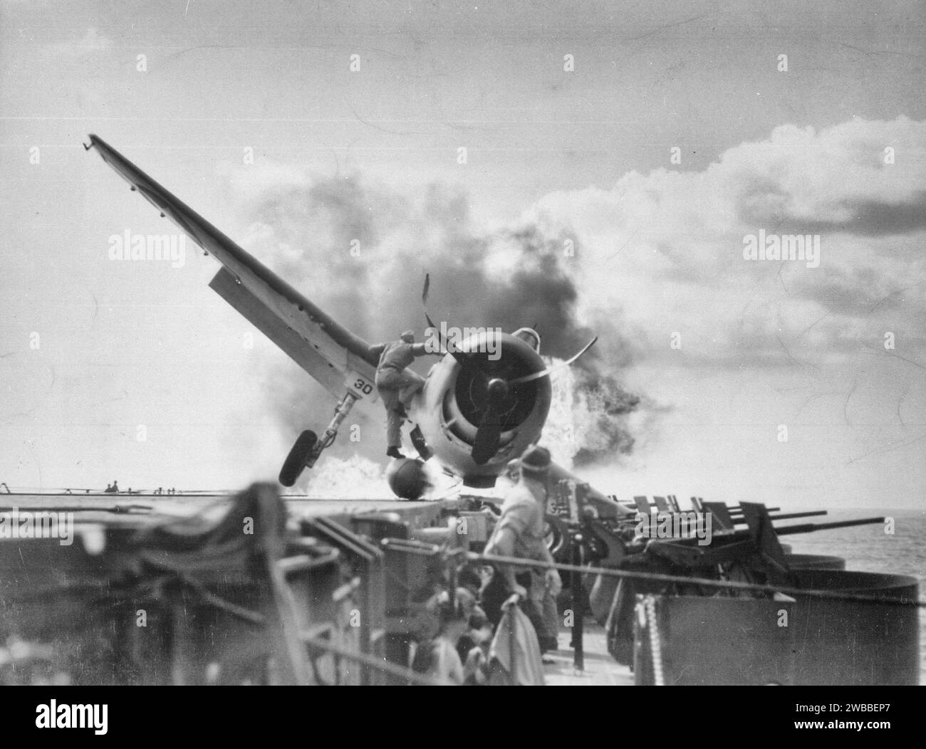 Sturzlandung der F6F auf dem Flugdeck der USS ENTERPRISE auf dem Weg zum Angriff auf Makin Island. Lieutenant Walter Chewning, Katapultoffizier, stürmt die Seite des Flugzeugs hoch, um Pilot Ens zu unterstützen. Byron Johnson, aus dem flammenden Cockpit während des Zweiten Weltkriegs Stockfoto