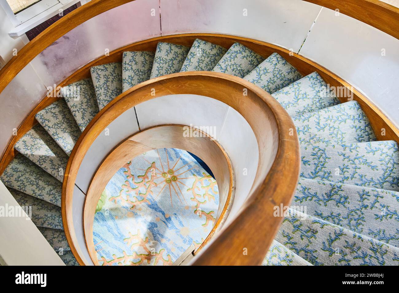 Elegante Wendeltreppe mit gemustertem Teppich und Mosaikdetail, Blick von oben nach unten Stockfoto