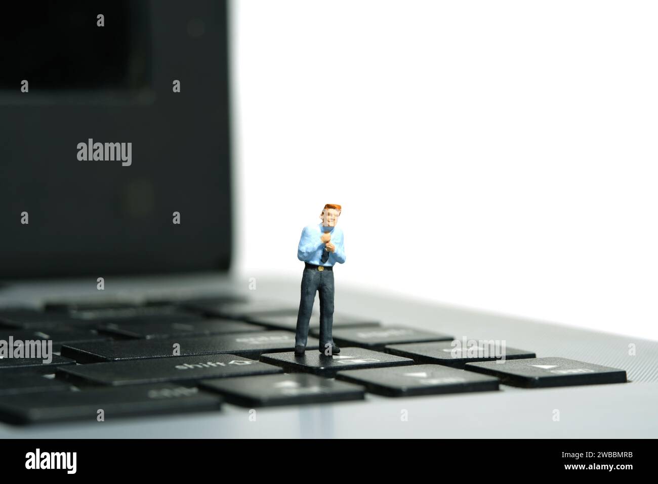 Miniatur-Kleinkinder-Spielfiguren-Fotografie. Ein Geschäftsmann, der sich bereit macht, rechtfertigt die Krawatte, die über der Notebook-Tastatur steht. Isoliert auf weißem Hintergrund Stockfoto